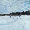 Painting of two people playing shinny frozen pond.